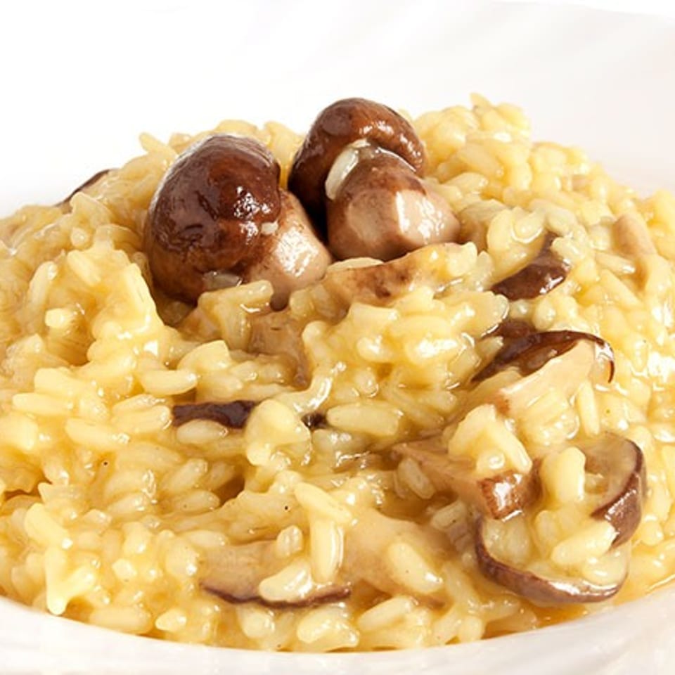 Creamy mushroom risotto served on a white plate, topped with sliced browned mushrooms.