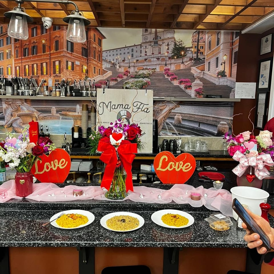 Mama Fla restaurant counter decorated with flowers, heart-shaped Love signs, three plated dishes, and a Rome’s Spanish Steps mural.