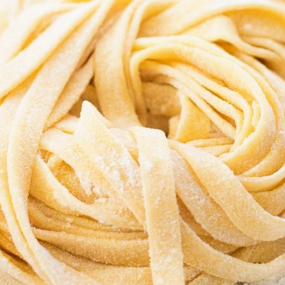 Close-up of fresh homemade fettuccine pasta noodles dusted with flour on a light surface.