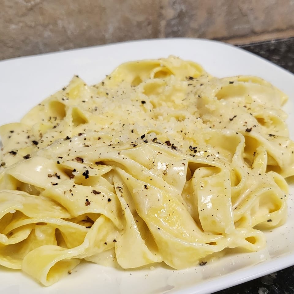 Creamy folded pasta topped with grated cheese and cracked black pepper on a white rectangular plate.
