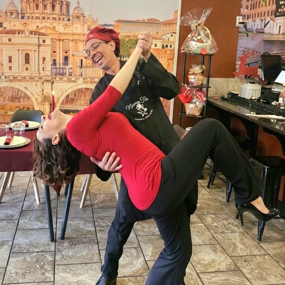 Restaurant staff member playfully dips a woman in front of a mural depicting St. Peter’s Basilica.
