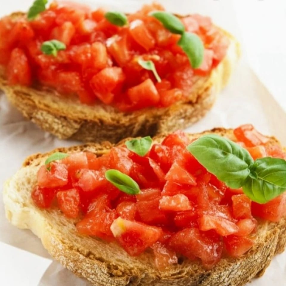 Two slices of toasted rustic bread topped with diced tomatoes and fresh basil leaves.